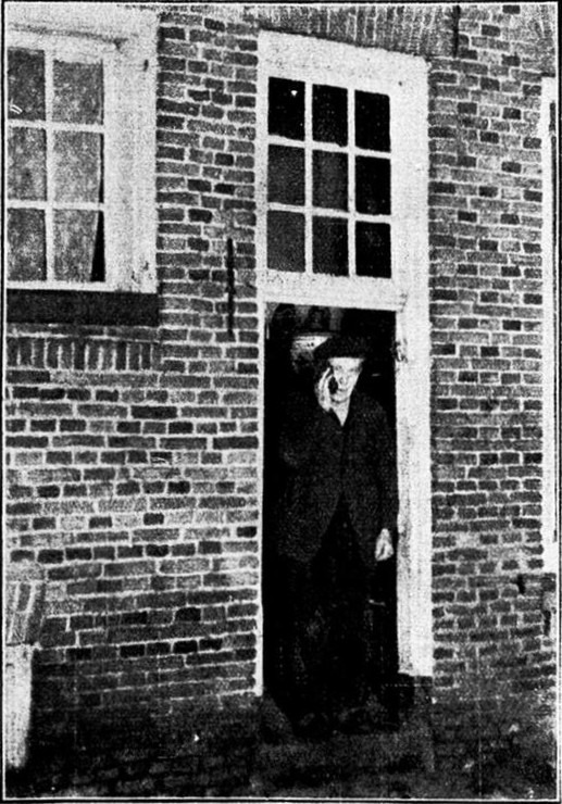 De entree van een der oudste, merkwaardigste en tevens goedkoopste „scheersalons” van ons land: scheren 5, knippen 10 cent. — Een der vaste klanten verlaat den scheerwinkel, terwijl hij zich met zijn zakdoek de zeepresten van het gezicht veegt…